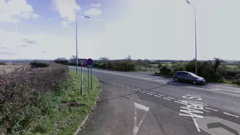 Google Stretch of road with a car on, next to road signs and near by grass.