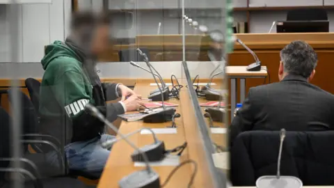 Alamy Live News The defendant, a suspected member of Hezbollah, sits behind a glass wall before the start of his trial at the Higher Regional Court in Celle.