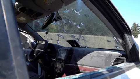 A car windshield with bullet holes, seen through the front passenger door window