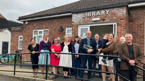 Supporters of Woodston Library standing in front of the small red brick building in Peterborough 