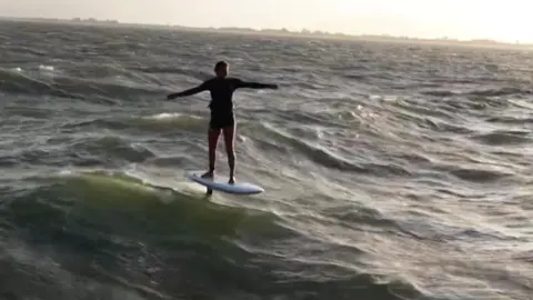 Guy Bridge A person balances on a hydrofoil board, gliding above choppy waves with arms outstretched as the wind ripples across the open sea.
