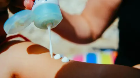 Getty Images Woman putting suntan lotion on her child at a sunny day in summer vacation. 