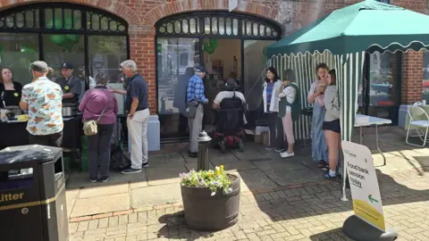 Alton Foodbank People speaking to Dexter and his mum behind the food counter and people gathered around talking outside the foodbank.