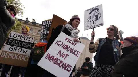 PA A woman holds a poster reading 'fight ignorance not immigrants' and another woman next to her has a sign with 'migration is not a crime'.