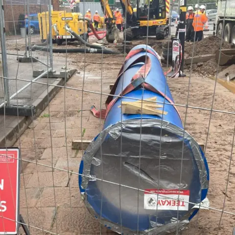 Severn Trent Water A large new blue pipe sitting on top of a road behind a metal fence