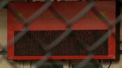 A big digital sign seen through the fence of Trenchard Lines telling people not to drink the water