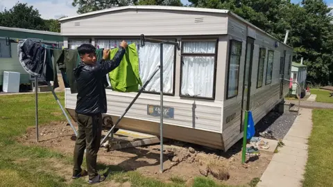 Nepalese worker hanging out washing at his caravan