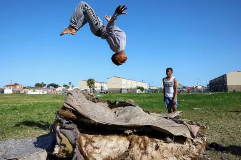 Reuters A boy plays on old mattresses in Hanover Park, an area affected by ongoing gang violence in Cape Town, South Africa, September 28, 2022