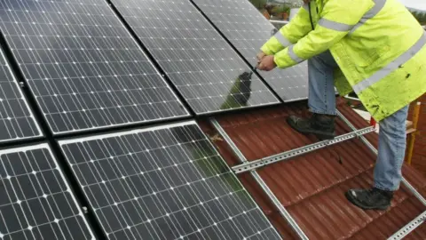 Niall Carson A man installing solar panels on a roof