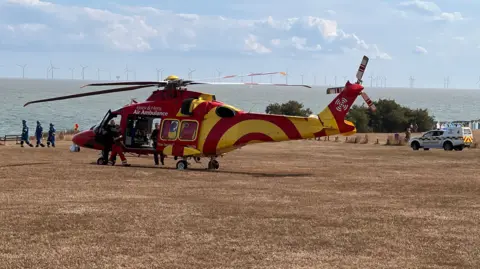 A red and yellow air ambulance on Frinton-on-Sea's Greensward - a large, open area of grass by the seafront.