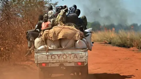 AFP A pick-up truck transporting people and goods drives past burning fields as it heads to Wau on January 31, 2020. 