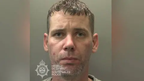 South Wales Police A mugshot picture of a man with short hair and grey stubble