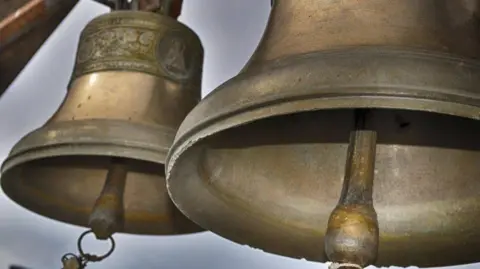 Two big church bells with their clappers underneath with a grey sky behind them