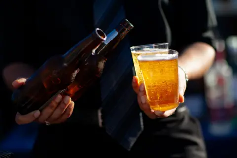 Person holding a beer and two glasses