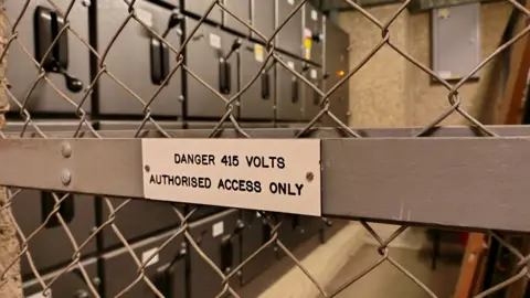 Simon Furber A warning sign stating: 'Danger 415 volts - Authorised Access Only'. The sign is on a gray panel with diamond wiring either side.