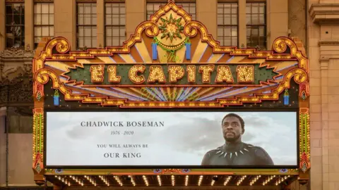 Getty Images The Disney El Capitan cinema in Los Angeles displays a tribute to Chadwick Boseman on its colourful marquee studded with fluorescent lights. A portrait of the actor in his Black Panther against a cloudy sky is displayed next to the text "Chadwick Boseman, 1976 - 2020, you will always be our king".