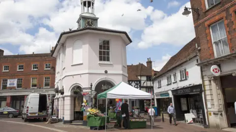 A stall in Godalming high street. It is next to a clock tower and there are shops and people in the street. 