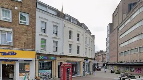 Terrace of buildings in Bournemouth with red phonebox at the front - most are flats on two storeys with shops below.