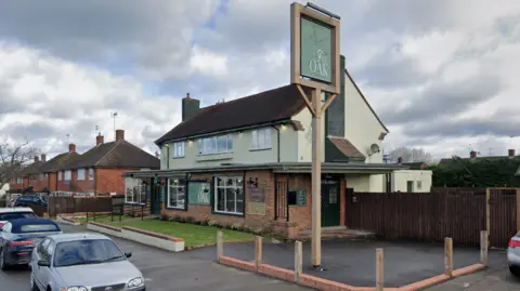 A brick double-storey pub with a sign reading "The Oak", which sits beside residential houses