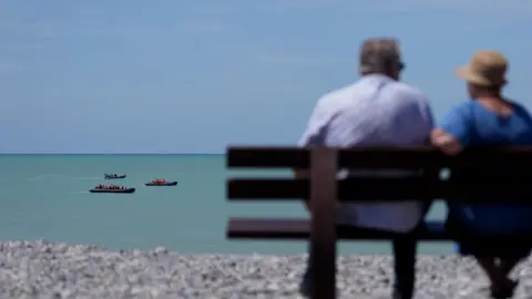 A couple watch two small boats hug the coastline near Ault in France as people thought to be migrants attempt to cross the Channel in June