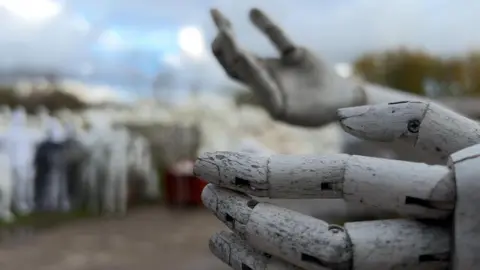 A zoomed view of a wooden mannequins hand, in the background is a mound of mannequins.