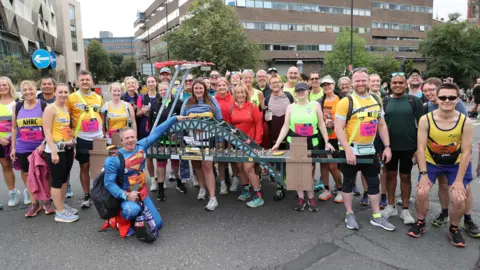 North News Dozens of people in running gear standing my model of green Tyne Bridge. They are all smiling and posing for the camera.