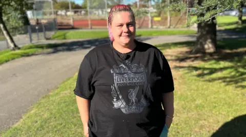 BBC Lorraine Parbury standing at a park wearing a black Liverpool top with coloured pink hair