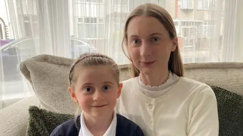 Faye and her mum Bex smile while sitting on a sofa at home