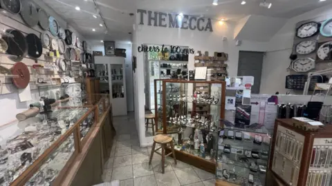 Shop with white walls tiled floor, wooden panelled jewellery stands and clocks on walls