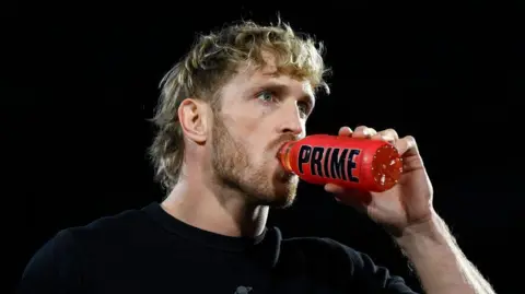 Logan Paul, pictured from the shoulder up, drinking a red bottle of Prime