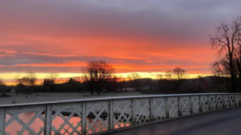 BBC Weather Watcher Stewski Pangbourne, Berkshire sunrise seen from a bridge looking across a meadow covered in frost