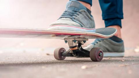 A right foot in blue trainers on a skateboard, with the left foot on the ground behind