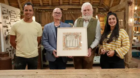 Ricochet/BBC/The Repair Shop Will Kirk, John Beard, John Greaves and Angelina Bakalarou on set at The Repair Shop. The two Johns are holding the framed serviette.