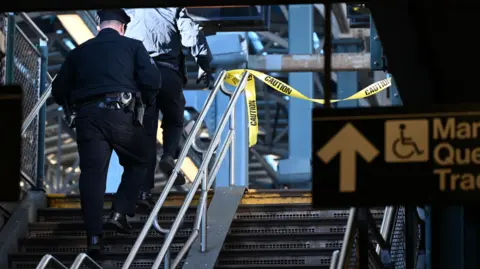 Getty Images Police investigate the Coney Island-Stilwell Avenue station in Brooklyn after a woman on a subway car was set on fire and died. A police officer can be seen walking up the stairs with yellow police tape flashing in the distance