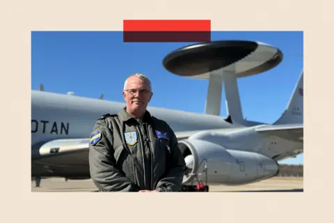 AWACS Dep Commander Andy Turk stands in front of a plane
