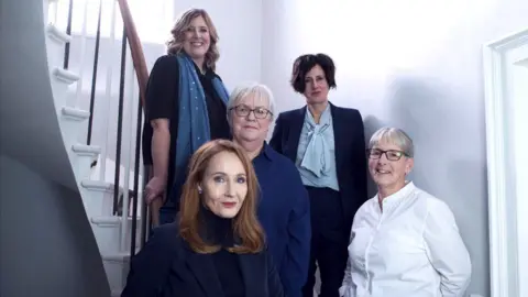 Beira's Place A group of women sitting on a staircase in a room with grey walls 