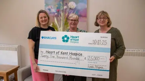 Heart of Kent Hospice Three women holding an oversized cheque. The cheque is for £25,000.