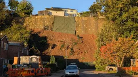 A view similar to that above but taken at the end of the main work, showing extensive pinning work to the top of the cliff, with houses visible above