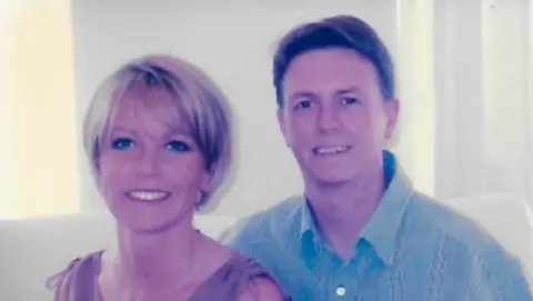 Family handout Mr Scott's sister has short blonde hair and is standing on the left-hand side of the picture wearing a pink or beige coloured top. Mr Scott is wearing a blue collared shirt. Both are smiling.