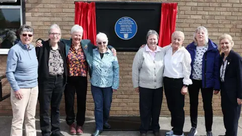 Members of the 1973 England squad who beat Scotland 8-0. The eight players are standing in front of a blue plaque which has been unveiled in Nuneaton. 