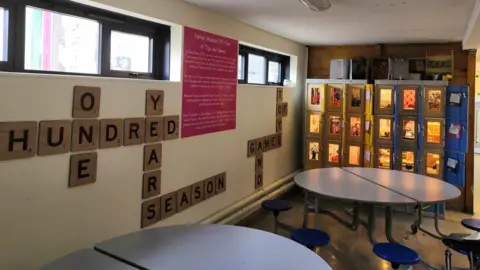 The Rumble Museum A view of the section of the corridor at the Rumble Museum where the lockers are displayed. There are tables and chairs in front. There are posts on the wall reading "One Hundred Years of Games and Toys"
