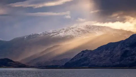 Getty Images Shafts of sunlight on hills dusted with snow and the loch in the foreground.