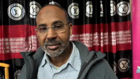 BBC News Abdikay is pictured wearing a blue striped shirt and grey coat 