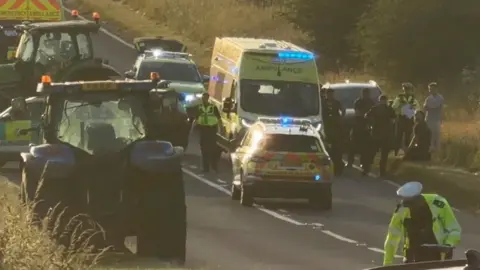 Emergency services at the scene on Copster Lane in Thurgoland. Police officers are examining the road, with ambulances and police cars. There are also two tractors on the route.