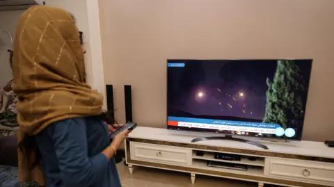 Getty Images A woman watches news about Iran's missile attack on Israel on television in Iran