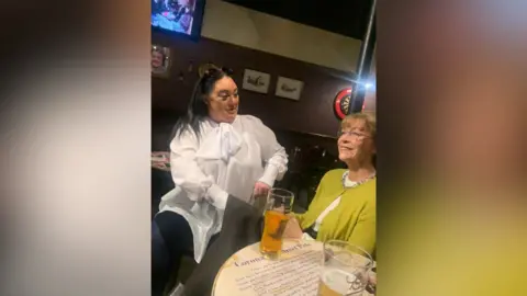 Handout Michelle Robinson sits with a waxwork of Deirdre Barlow in a replica of the Rovers Return Inn. She wears a white shirt and black leggings