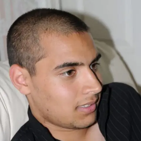 Nishat Siddiqi A smiling young man wearing a black shirt with short hair laying on a white pillow