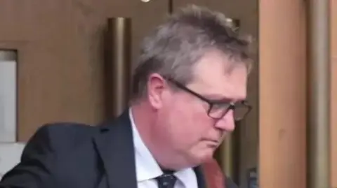 A man with short grey hair and glasses wearing a suit