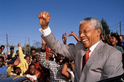 Nelson Mandela raises his fit in the air as he is surrounded by a crowd of young South Africans
