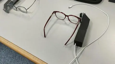 University of Plymouth A technical device with a see-through screen attached sits beside a pair of glasses on a white desk.